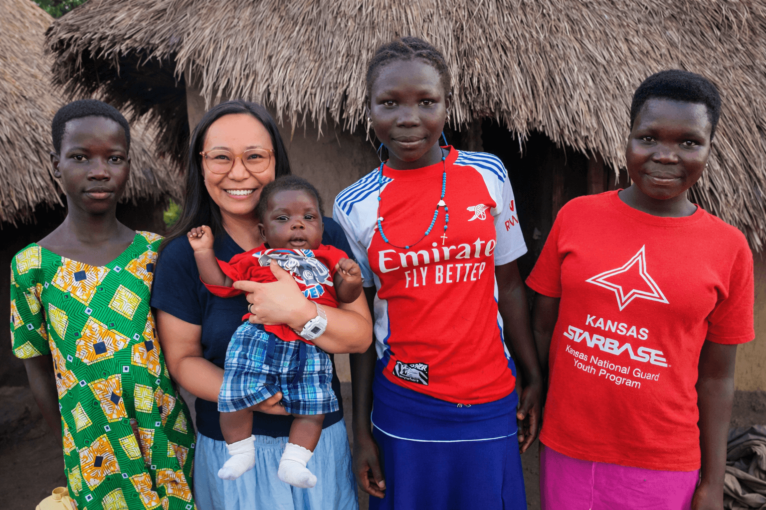 Asian woman and family standing in front of a hut